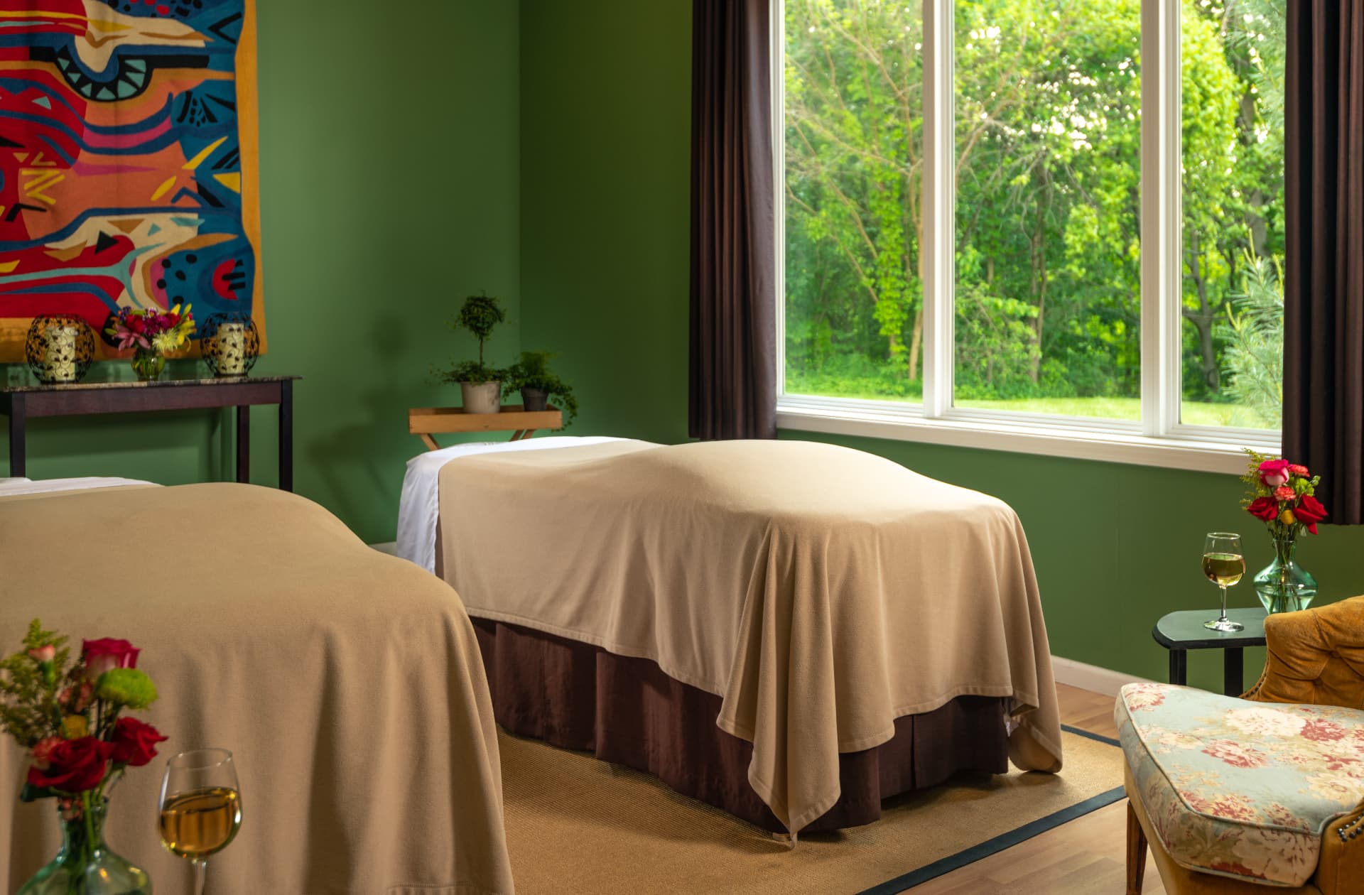A calming spa room featuring two massage tables and large windows overlooking greenery.