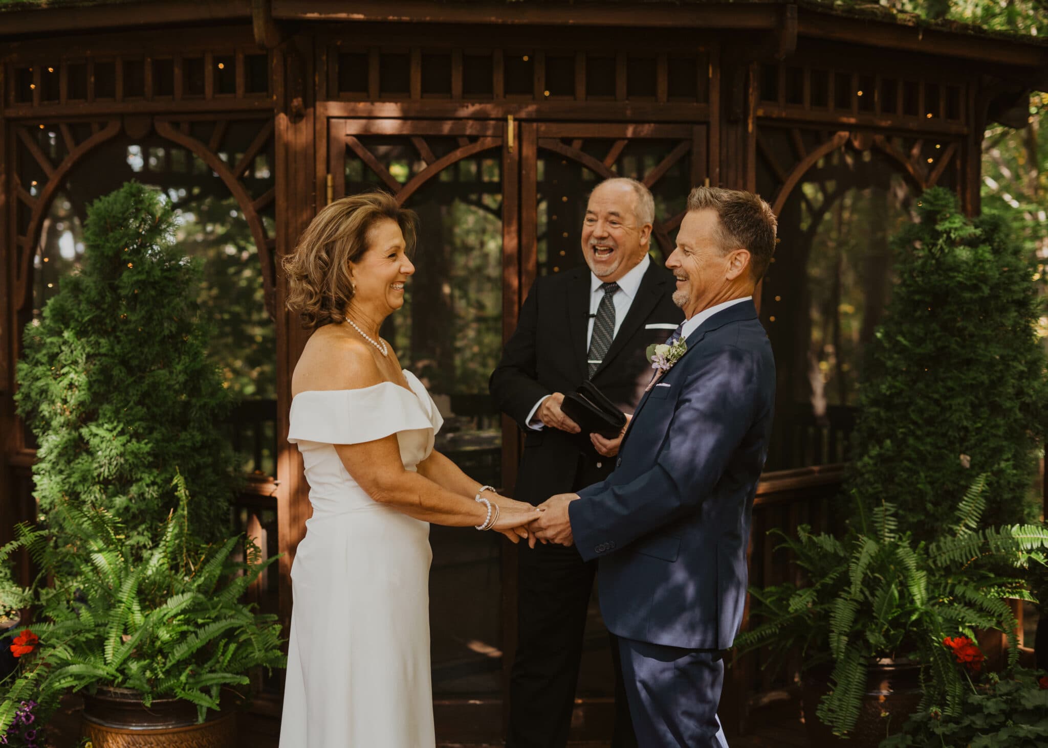 A couple exchanges vows with a celebrant in a decorative outdoor setting.