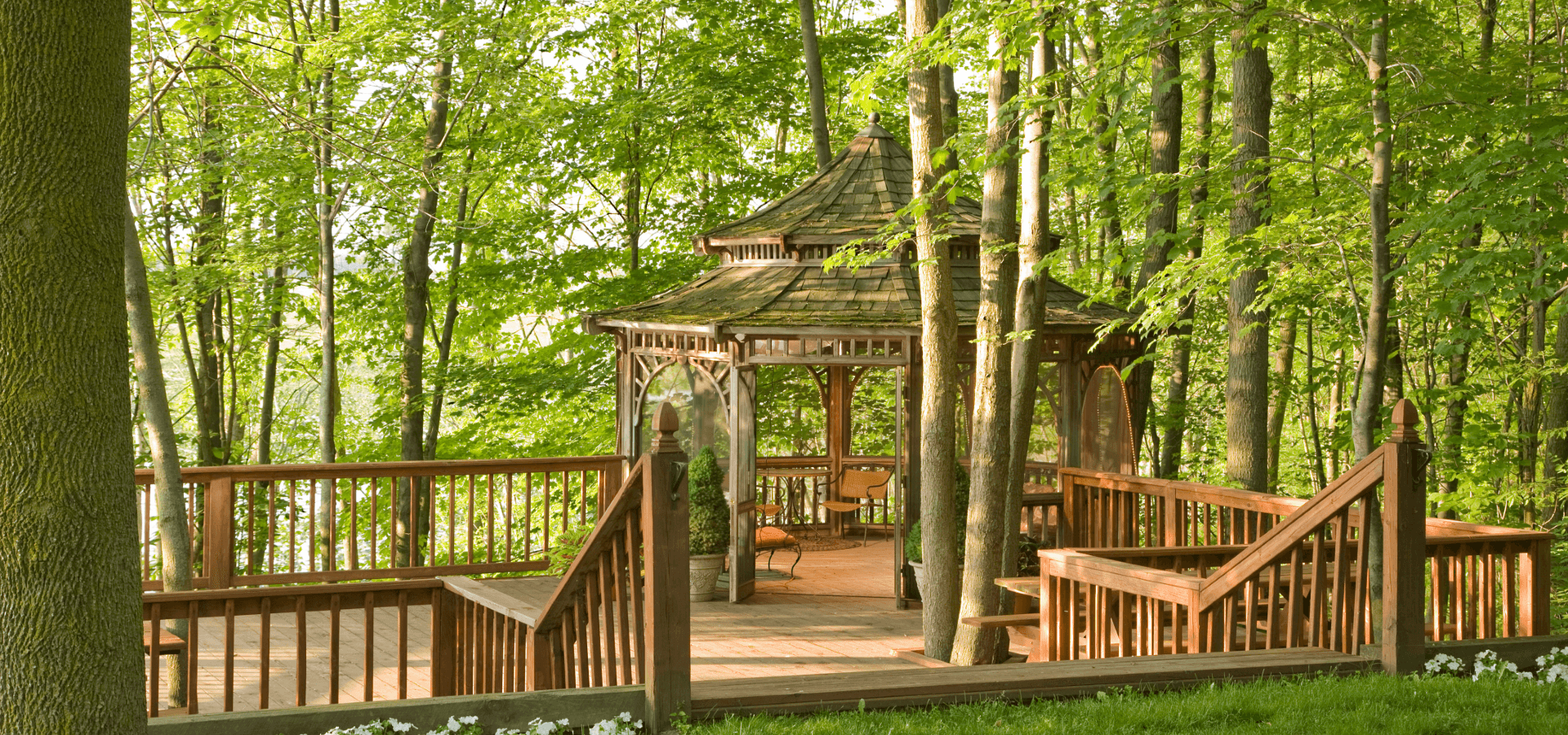 A wooden gazebo surrounded by lush greenery and trees.