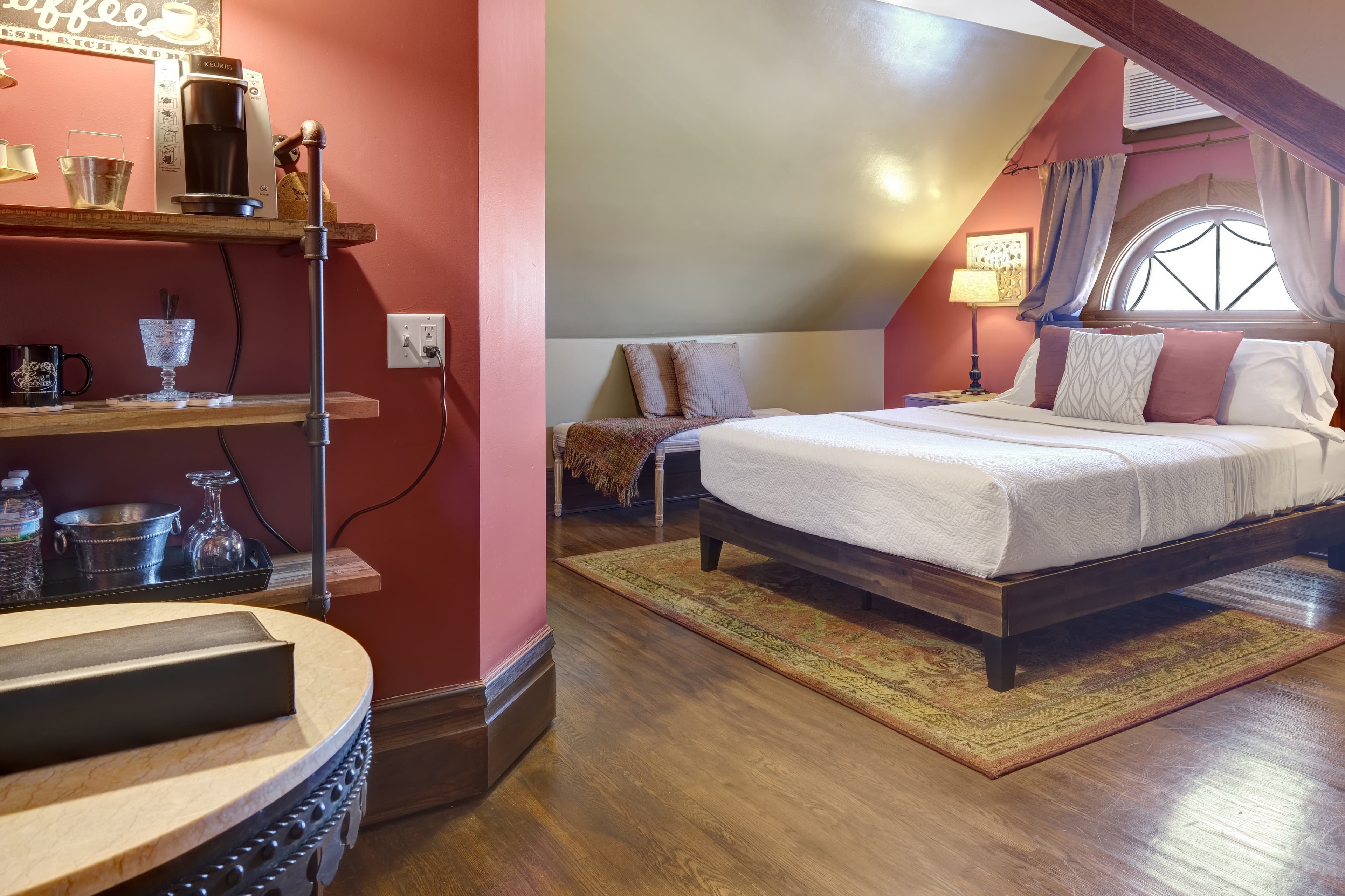 Room with a queen size bed, angled ceilings with a unique picture window.