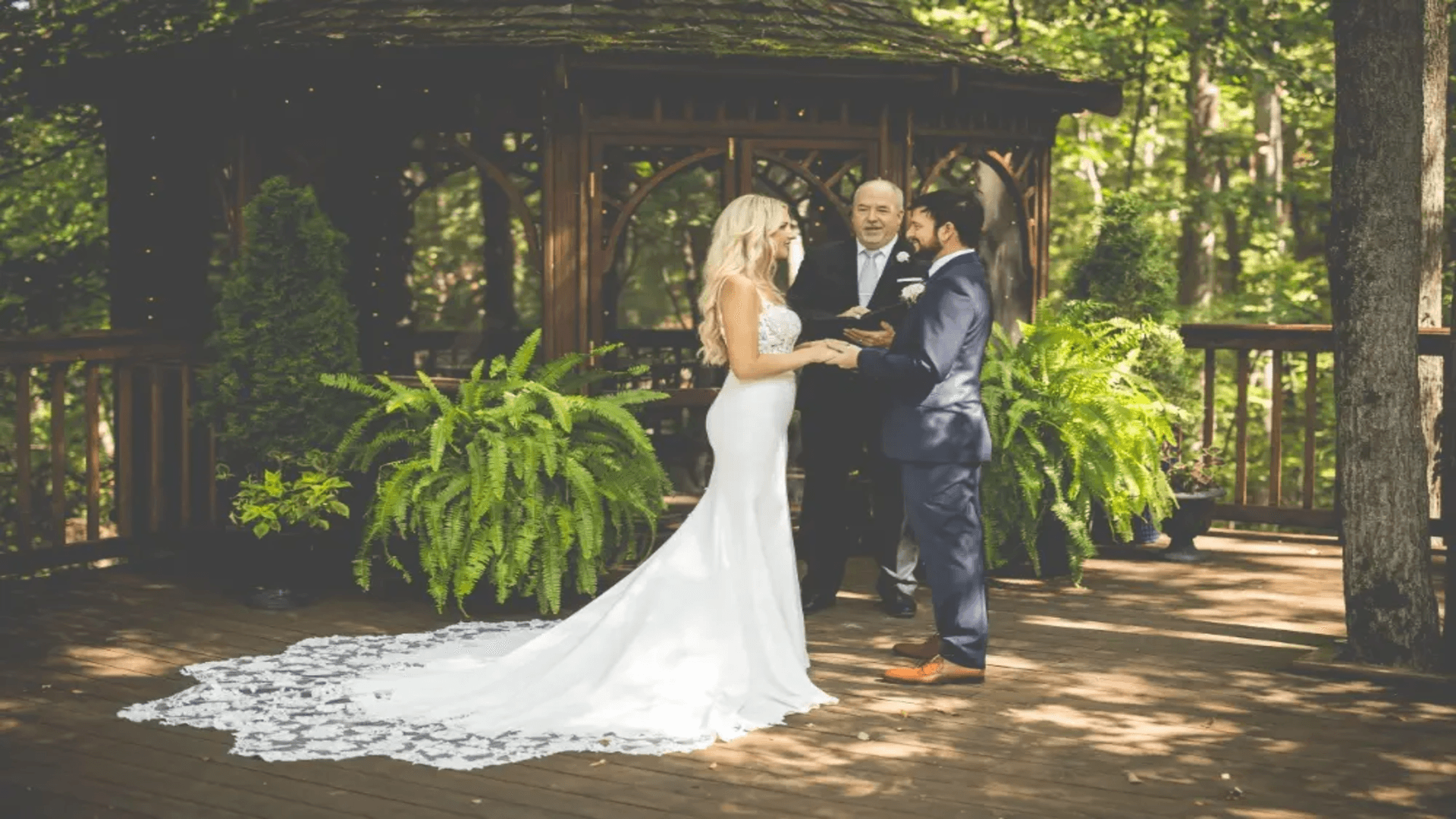 A couple exchanging vows under a gazebo in a lush outdoor setting.
