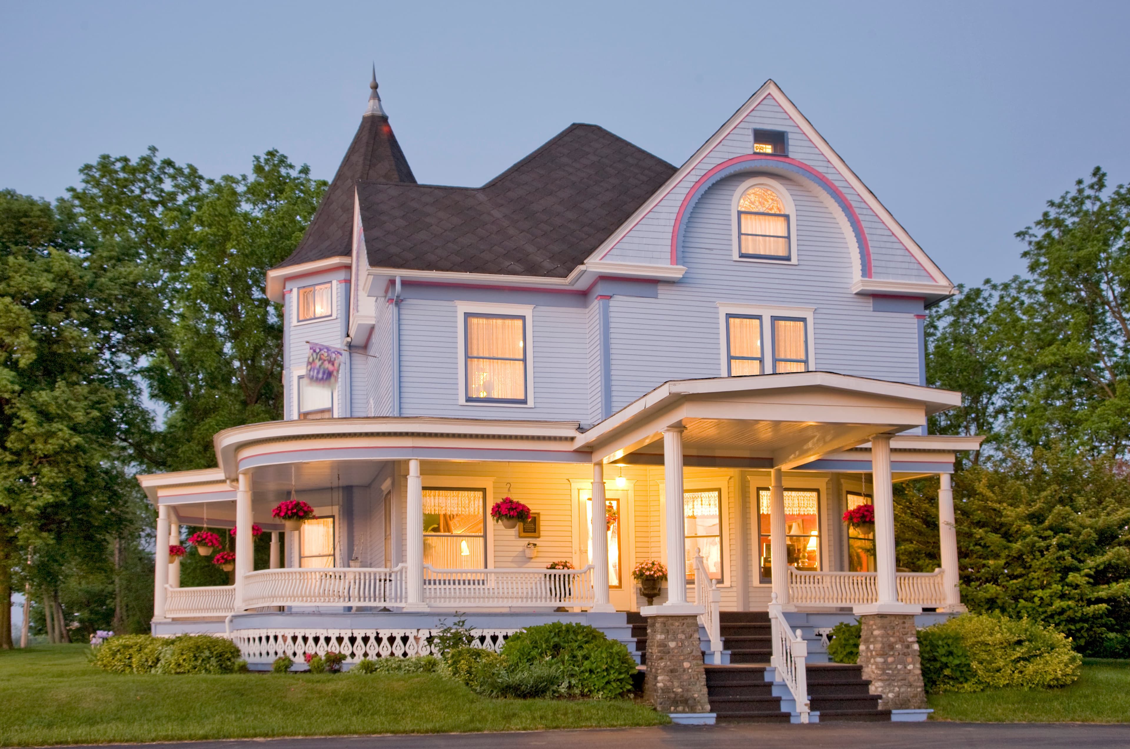 Victorian-style blue house with a wraparound porch and colorful flower decorations.