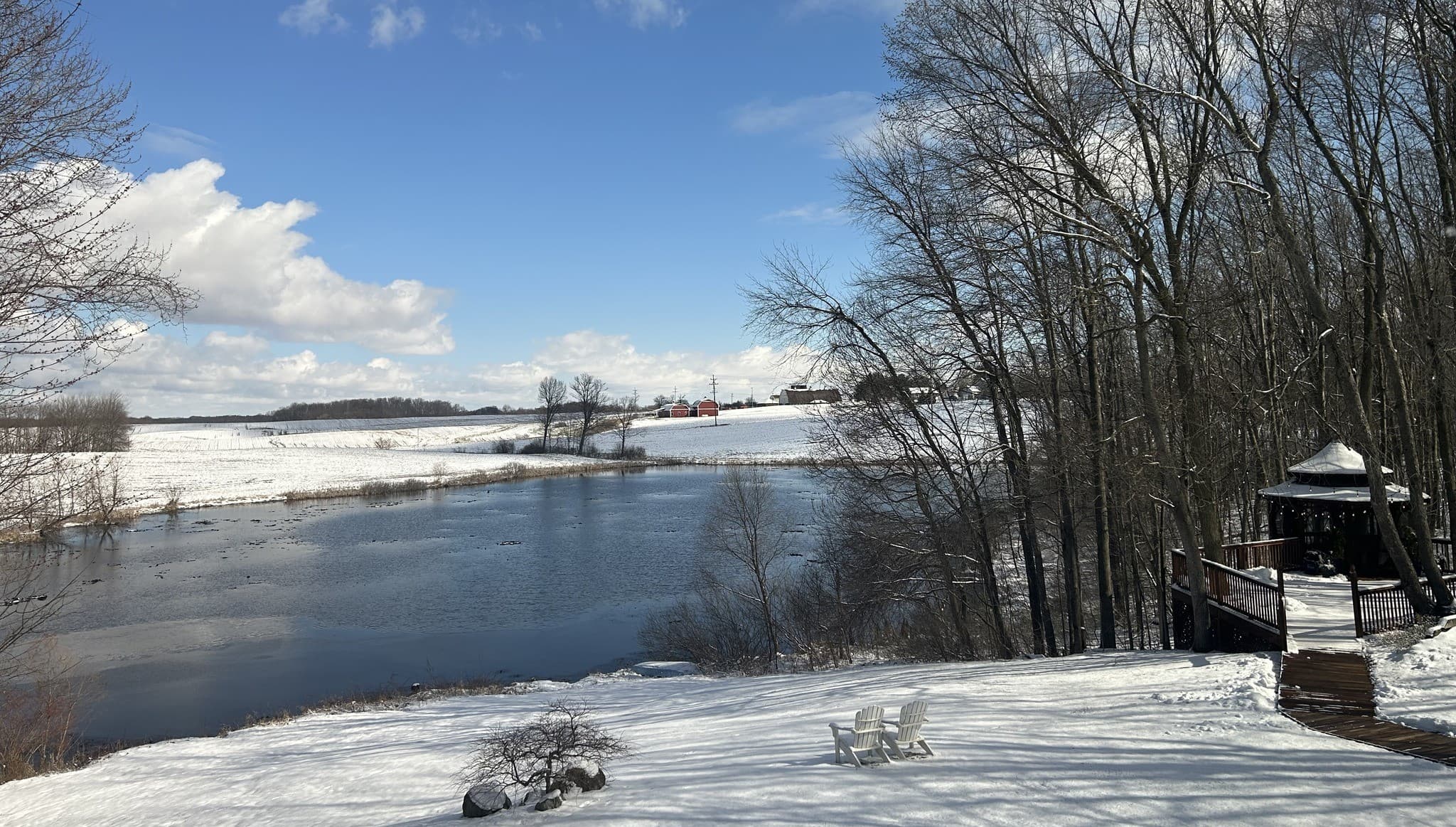 A serene winter scene featuring a snowy landscape, a frozen river, and bare trees under a bright blue sky.