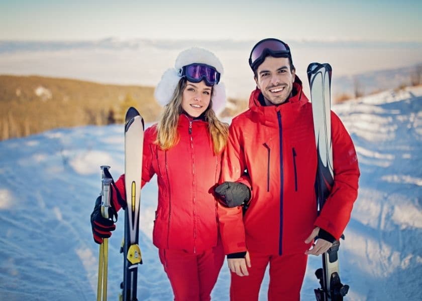A young couple in matching red ski outfits poses with their skis on a snowy mountain. A young couple in matching red ski outfits poses with their skis on a snowy mountain.