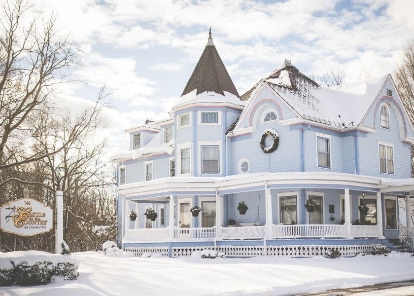 The exterior of Castle in the Country and the inn sign are surrounded by snow-covered ground. The exterior of Castle in the Country and the inn sign are surrounded by snow-covered ground.