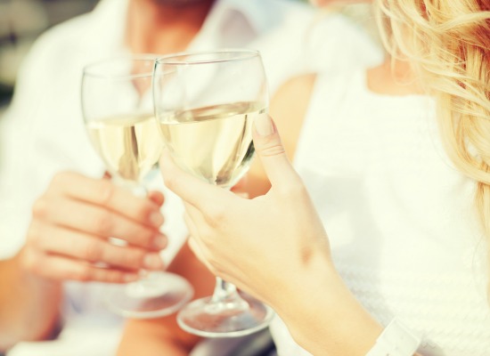 A couple dressed in summer, breezy white clothes toasting glasses of champagne.