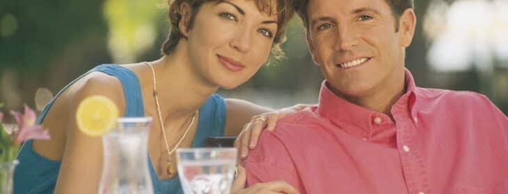 woman leaning on man's shoulder as they sit side by side in an outdoor dining spot