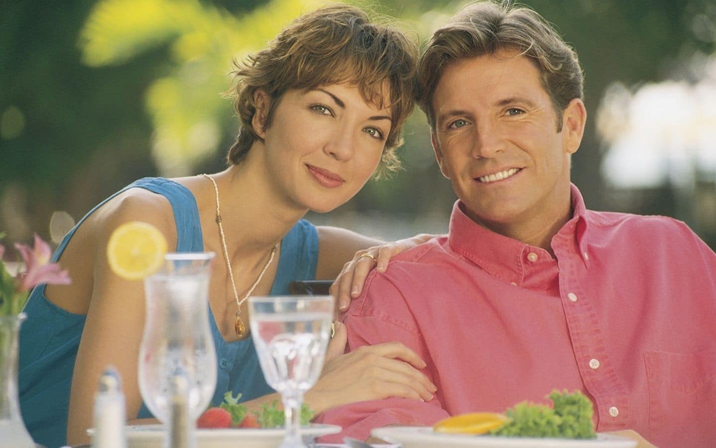 woman leaning on man's shoulder as they sit side by side in an outdoor dining spot