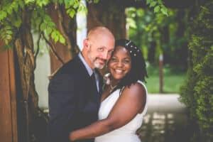 Wedding couple embrace under the pergola covered in green vines during the summer