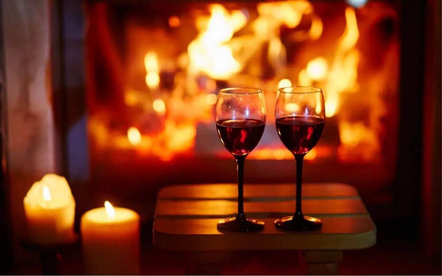 two goblets of wine with candles before a lit fireplace